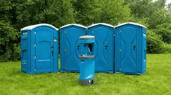 Four blue portable toilets and a matching hand washing station on grass near trees, a common sight at local outdoor events in Ann Arbor, MI