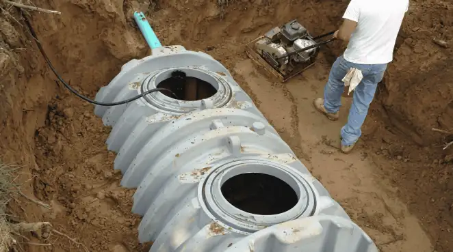 Septic tank installation showing a technician compacting soil around a new poly septic tank in an excavation pit in Ann Arbor, MI
